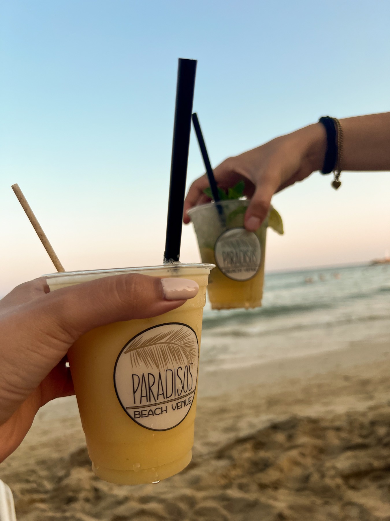 Two fruit cocktails held up beside the beach