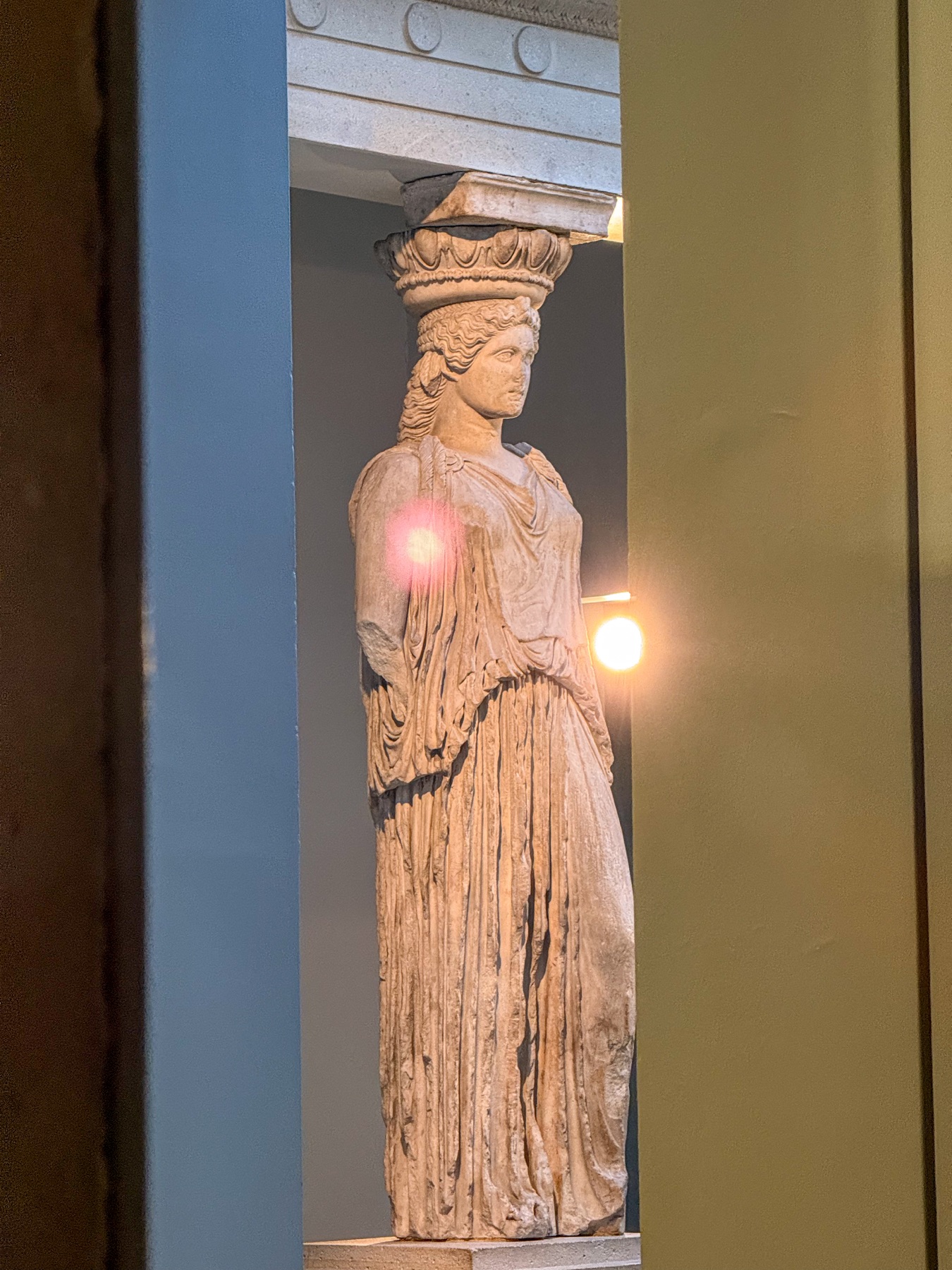 An ancient Caryatid displayed between coloured walls