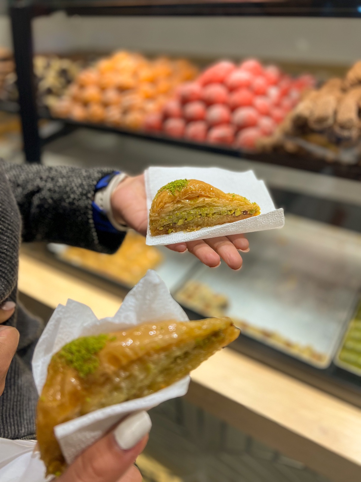 Two pieces of pistachio baklava held in a bakery